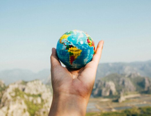 Ein kleiner Globus wird in der Hand gehalten vor einem Panoramablick.