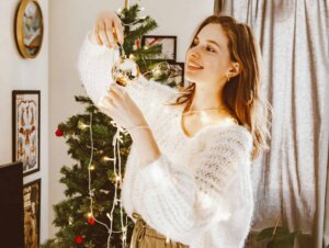 Eine Frau trägt einen weißen Strickpullover und hält eine Lichterkette in der Hand