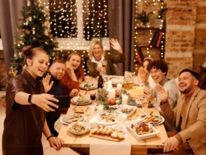 An einem langen Tisch sitzt eine Familie bestehend aus verschiedenen Generationen bei einer Weihnachtsfeier und macht ein Selfie.