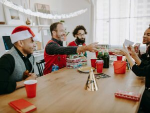 Eine Gruppe Freunde sitzt an einem Tisch und verteilt gegenseitig Weihnachtsgeschenke.