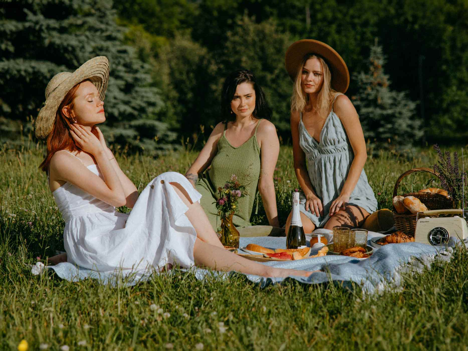 Drei Frauen sitzen auf einer Picknickdecke und tragen unterschiedliche Kleiderformen und Farben